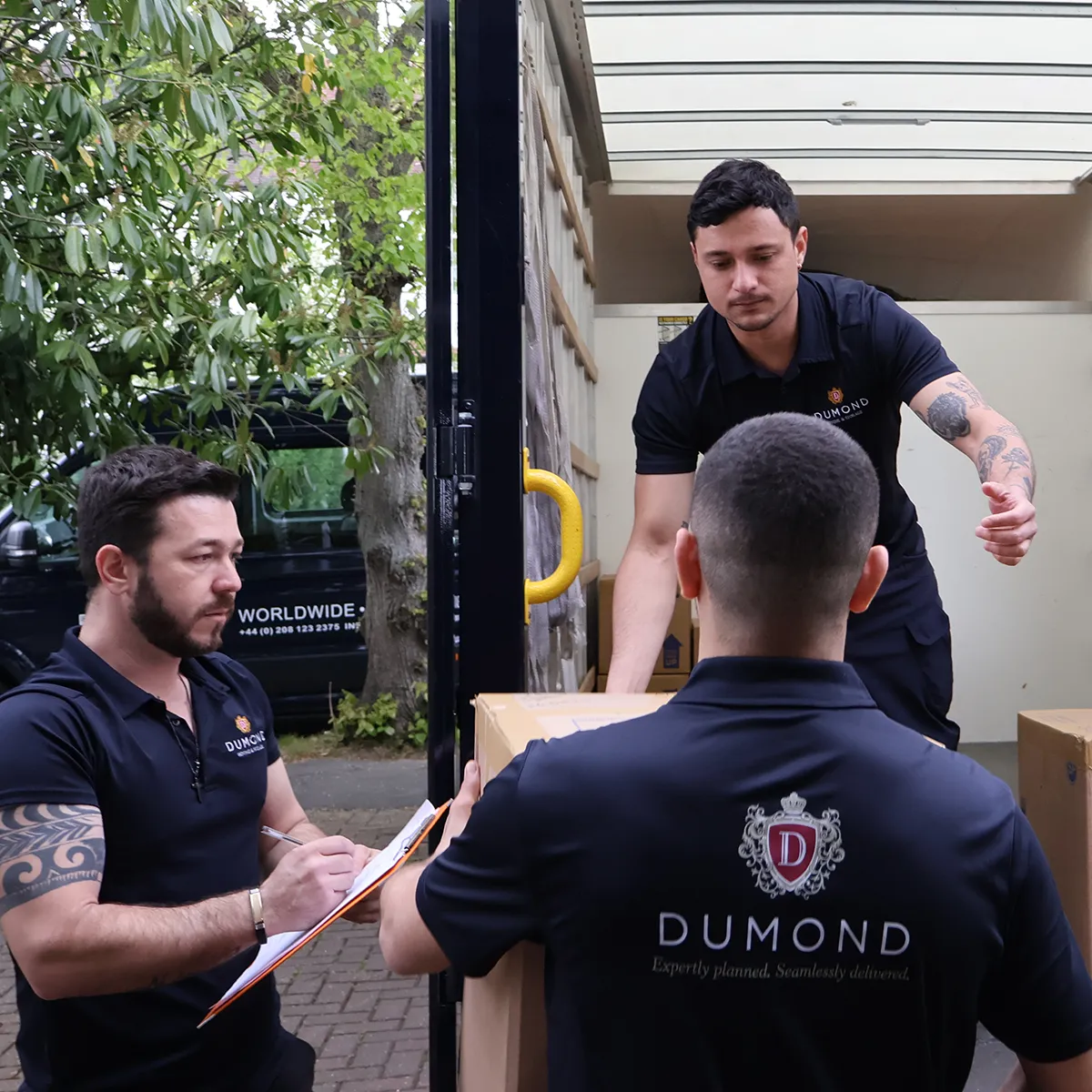 Three Dumond employees loading moving boxes into a van as part of a complex in-house logistics operation.