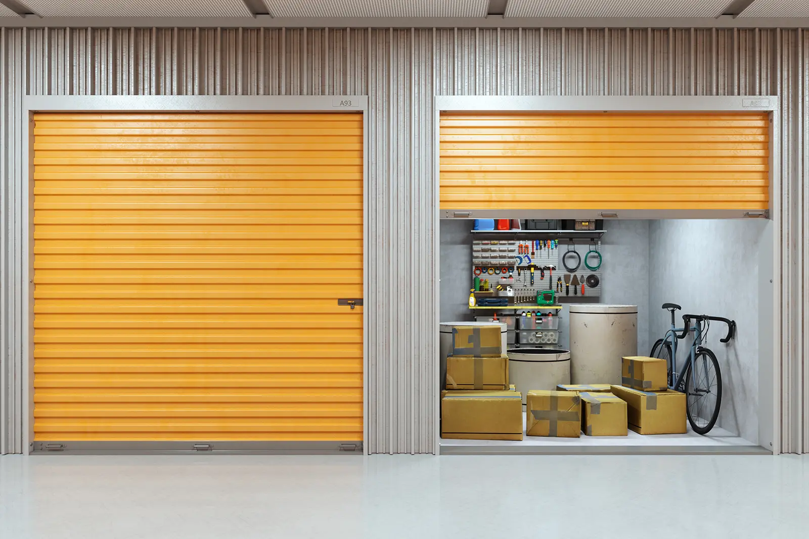 Two self storage units with orange roller doors, one open to reveal stacked cardboard boxes, a bicycle, appliances and a tool wall inside